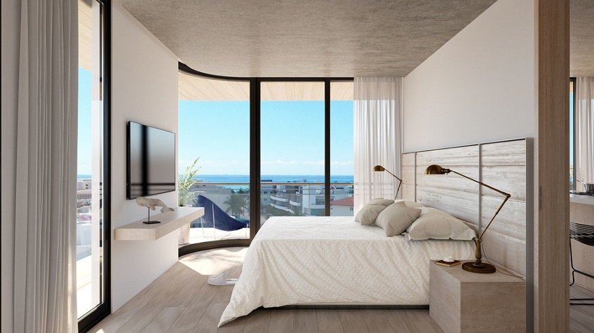 White bedroom with tv screen and tall balcony windows at The Boat Residence