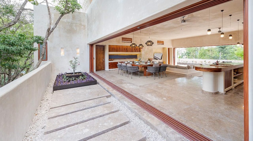 House with a large dining table and kitchen behind the wall size window at Aha Tulum