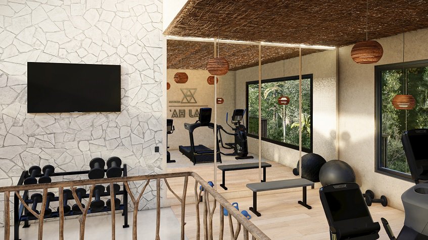 Indoor gym with mirrors and TV screen on the wall and windows at Elemental Tulum