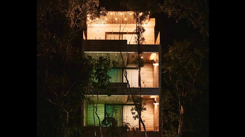 Illuminated balconies of three levels surrounded by trees at night at Zanza Tulum