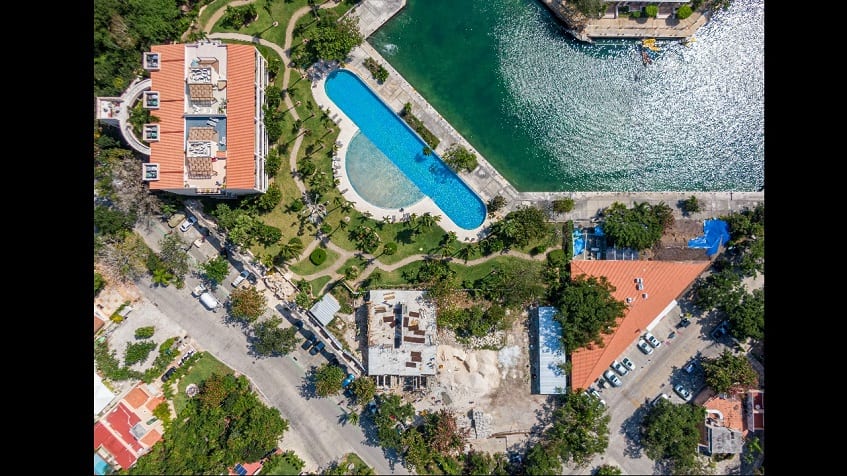 Aerial view of residential building with red roof and palm trees garden next to the pool, ocean at Secret Waters