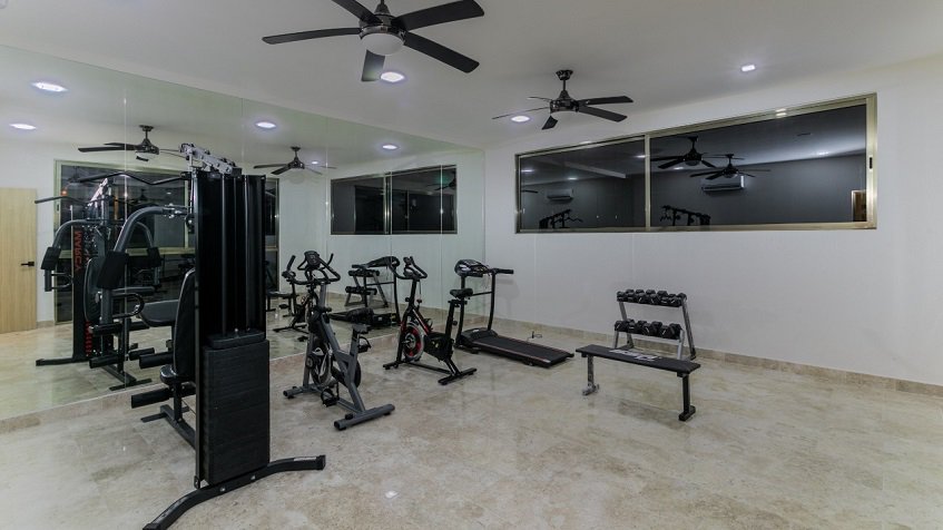 Gym room with many exercise tools, two small dark windows at Gaia Residence