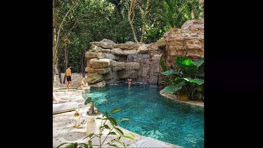 Pool in the garden with a woman under a waterfall at Kukun Tulum Condos