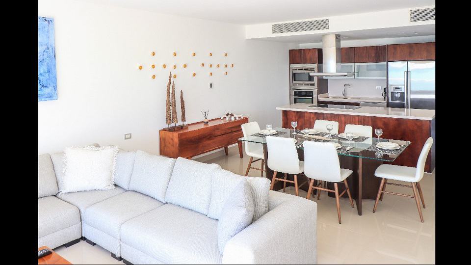 Sala de estar con sofá blanco y gran mesa de comedor junto a la cocina en Mareazul Beachfront Residences