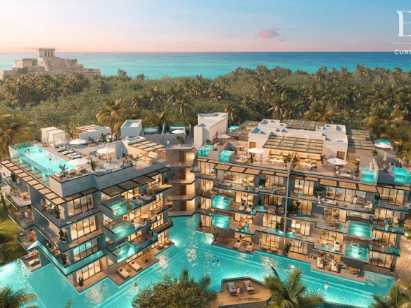 Vista de torres residenciales iluminadas con complejo de piscinas y vista al mar en Eos Tulum