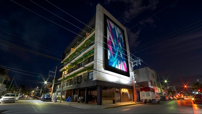 Colorida fachada de edificio de seis niveles en la noche Believe Playa Condos