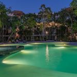 Illuminated pool surrounded by a tree garden at Yaaxlum Tulum