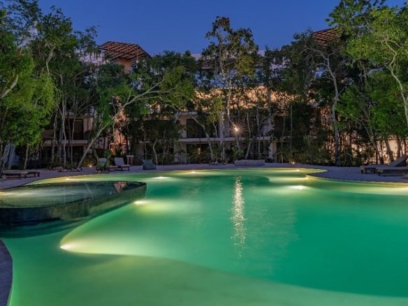 Piscina iluminada rodeada de un jardín de árboles en Yaaxlum Tulum