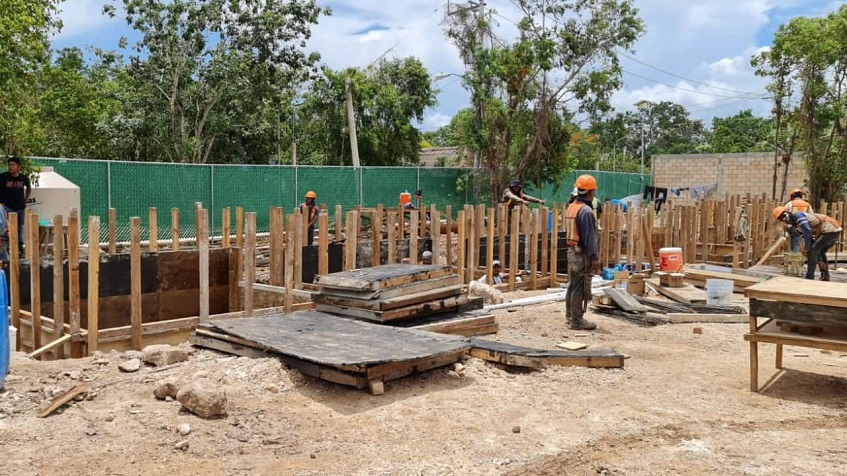 Construction area with workers arranging wooden poles inside the ground in Bacab Tulum