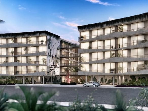 Fachada de edificio residencial con balcones y un auto que pasa por la calle Distrito Arte Tulum