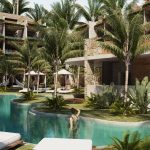 People swimming and hanging out around a pool and sundeck surrounded by vegetation at Naia Tulum