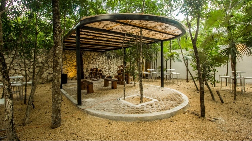 Gimnasio al aire libre cubierto con techo rodeado de un jardín de árboles con mesas y sillas en Kantuun Tulum