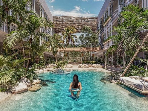 Piscina en planta baja rodeada de edificio residencial, una mujer dentro del agua en Jungle Paradise Tulum