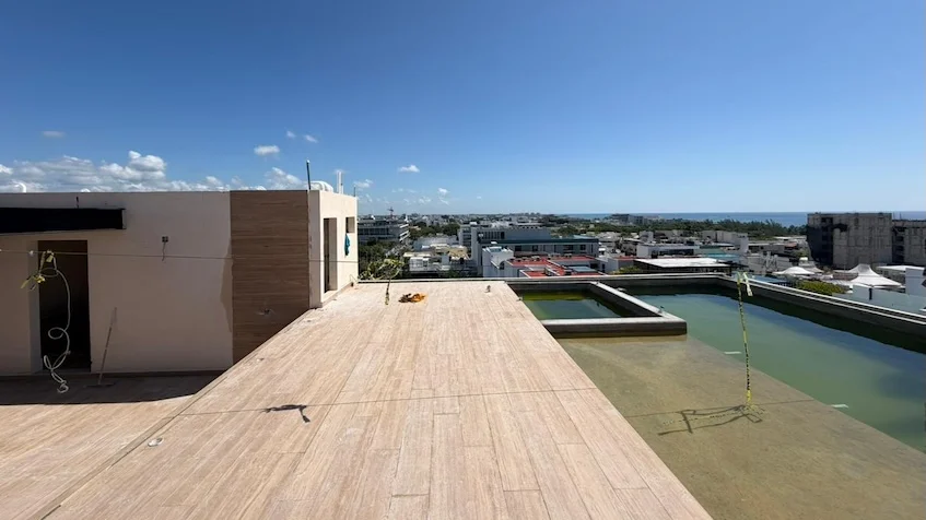 Vista de rooftop que incluye un área de cubierta de madera tipo deck, una piscina al aire libre, camastros y una vista panorámica hacia la zona urbana y el mar de Distrito Playa