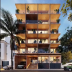 Fachada de un edificio, una palmera y 3 autos estacionados en Ikuku Playa del Carmen