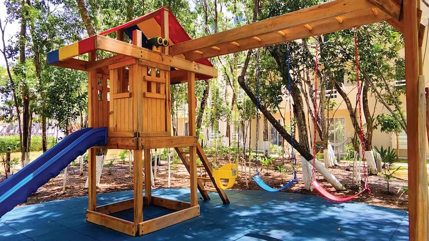 Zona de juegos infantil con columpios y piscina de fondo en La Selva Residences