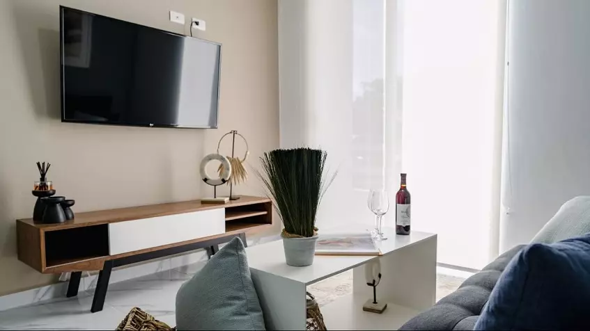 A room with a gray sofa, a wooden furniture and a TV set at La Selva Residences