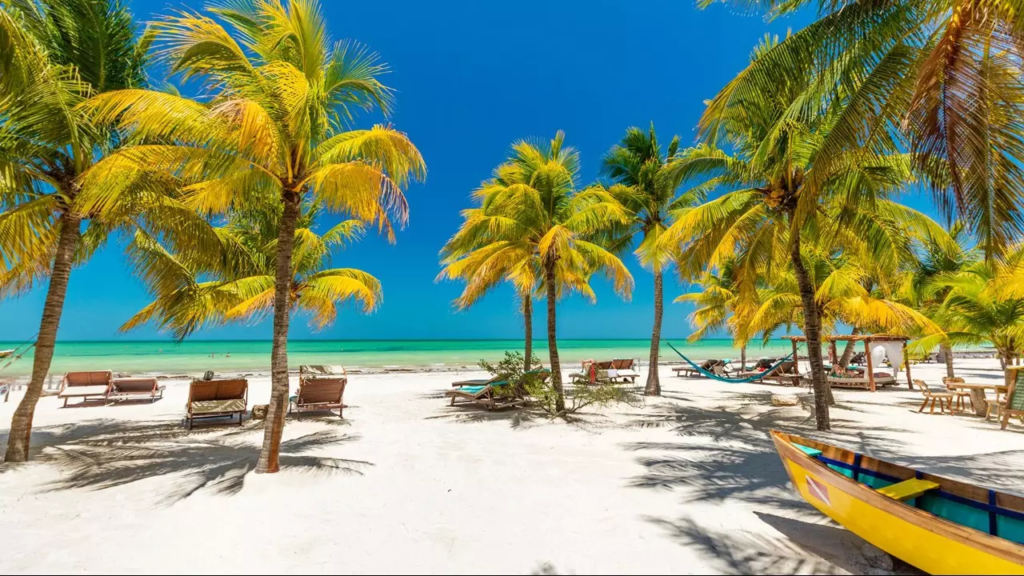 Unas palmeras, una lancha amarilla, y camastros en una Playa