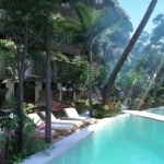 A pool area with lounge chairs and surrounding gardens at Natura Tulum