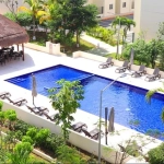 Vue sur une piscine avec palapa, chaises longues et jardins environnants à Aldea Tulum Plus