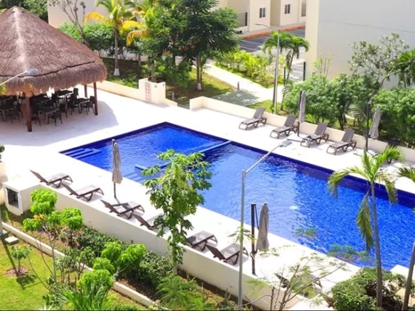 Vista de una alberca con una palapa, camastros y jardines alrededor en Aldea Tulum Plus