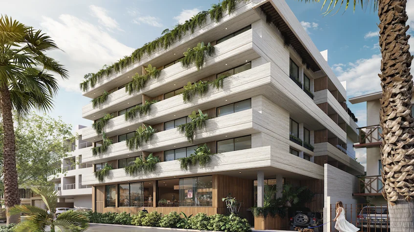 Fachada frontal del edificio que incluye una estructura arquitectónica moderna de varios niveles con balcones corridos decorados con vegetación colgante, acabados en tonos claros y piedra, y un acceso principal de Luum Kan Cancún