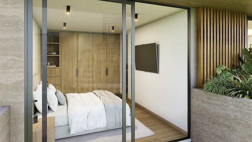 Recámara con vista a la terraza que incluye una cama tendida, clóset de madera con puertas batientes, televisión montada en la pared y una puerta corrediza de cristal con acceso al balcón de Luum Kan Cancún