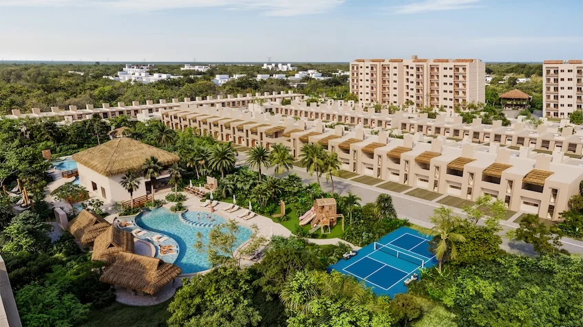 Vista aérea que incluye un complejo de edificios residenciales, una alberca central con palapa y tobogán, una cancha deportiva azul, áreas verdes y palmeras de The Reserve By Gran Selva Puerto Morelos.
