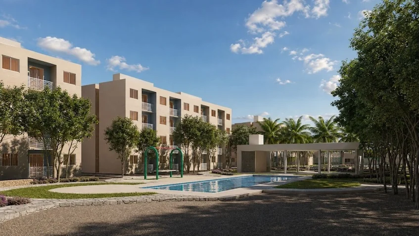 Área de alberca y jardín que incluye una piscina, amplias áreas verdes, un área de juegos infantiles, un edificio residencial de varios niveles, una casa club y árboles de Vía Verde Playa del Carmen,