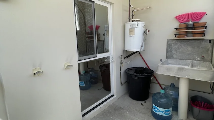Área de lavado que incluye un lavadero, un calentador de agua, garrafones de agua, botes y una puerta de cristal de Jardines de Mayakoba Playa del Carmen.