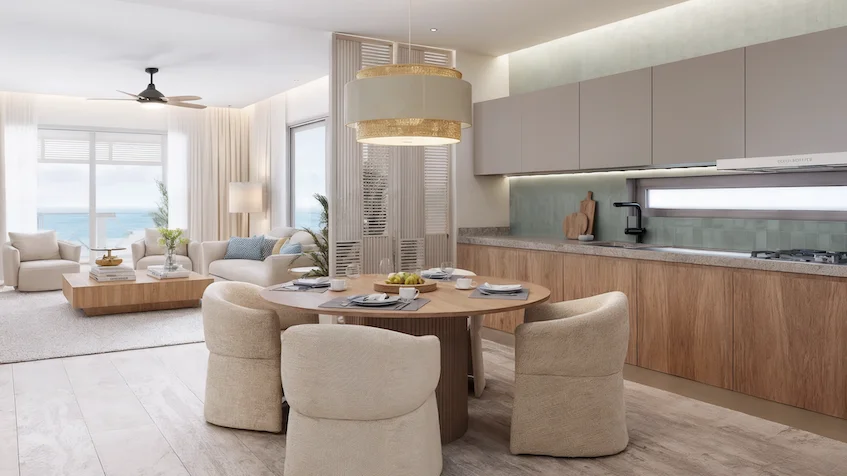 Sala, comedor y cocina que incluye una mesa redonda con sillas, una lámpara colgante, gabinetes de madera, un sofá al fondo, ventanales con vista al mar y un ventilador de techo de Isola BLU Isla Mujeres.