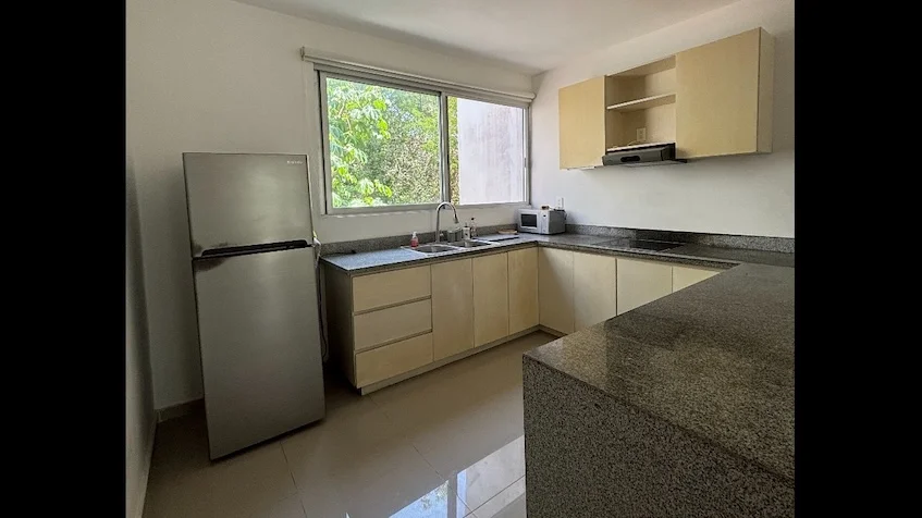 Cocina que incluye una amplia barra, gabinetes, un refrigerador, un microondas y una ventana con vista a áreas verdes de Condominio Uxmal Playa del Carmen.