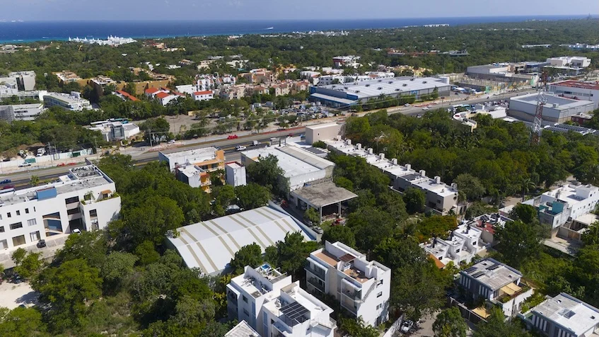 Vista aérea que incluye edificios residenciales, vialidades, extensas áreas verdes y el mar al fondo de Condominio Uxmal Playa del Carmen.