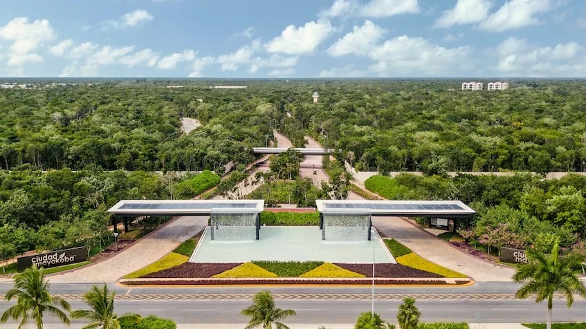 Vista aérea de la entrada principal que incluye amplias estructuras de acceso, fuentes de agua, vialidades y áreas verdes de Entre Bosques Mayakobá Playa del Carmen.