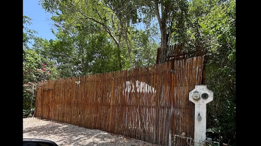 Vista de la entrada que incluye una cerca rústica de madera, un medidor de luz, árboles, abundante vegetación y un cielo despejado de Terrenos en Chemuyil.