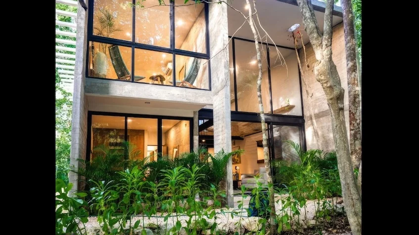 Fachada lateral que incluye un diseño arquitectónico contemporáneo de varios niveles, revestimiento de piedra, balcones con barandales de cristal, vegetación colgante de Senzik Tulum
