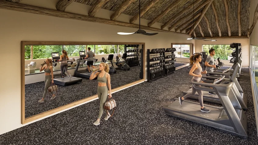 Vista interior de gimnasio que incluye un área de pesas y caminadoras, un gran espejo en la pared, un techo con estructura de madera de The Origin by Gran Selva Puerto Morelos.
