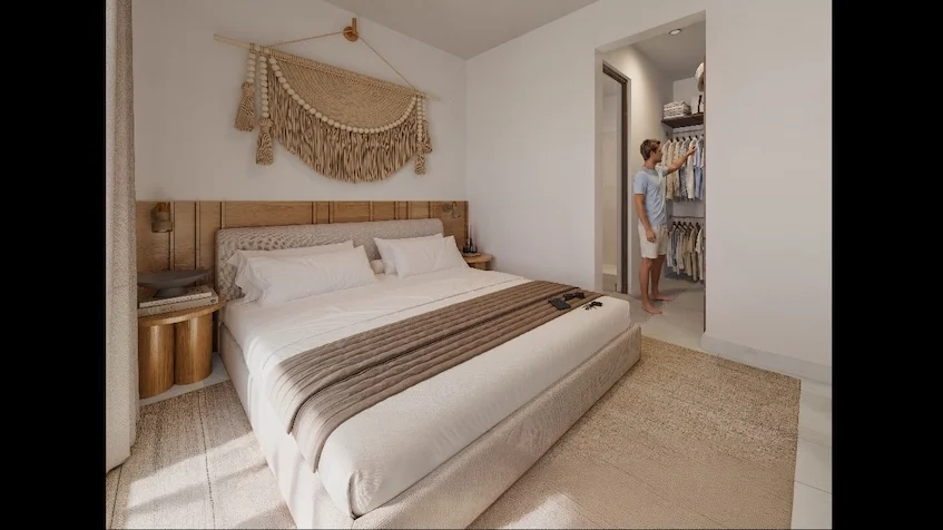 Interior de recámara que incluye una cama con cabecera de madera y decoración textil, un buró con lámpara y vestidor abierto al fondo de The Reserve By Gran Selva Puerto Morelos.