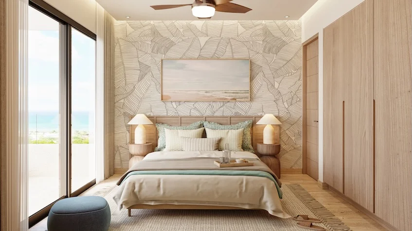 Recámara luminosa con cama matrimonial con cabecero de madera mesas de noche con lámparas un puf azul junto al ventanal con vista al mar, armario empotrado de madera y ventilador con iluminación en el techo de Village Blu Puerto Morelos