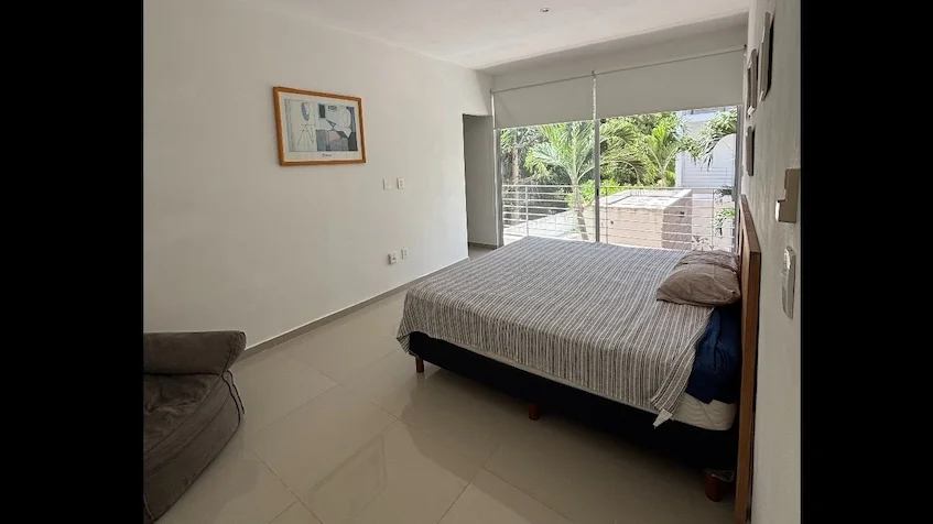 Recámara que incluye una cama, un sofá, un cuadro decorativo y un amplio ventanal con vista a áreas verdes de Condominio Uxmal Playa del Carmen.