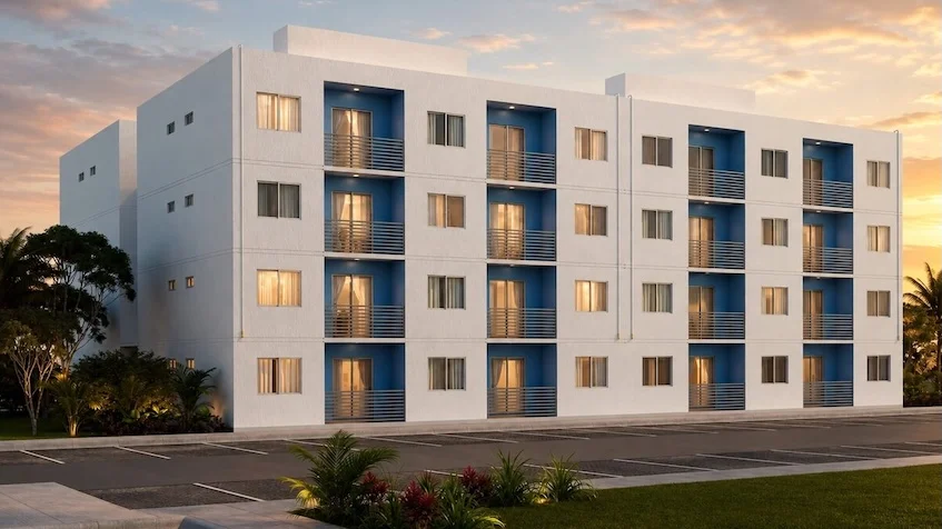 Vista exterior de edificio que incluye una fachada blanca con balcones azules, un área de estacionamiento, áreas verdes  de Vía Verde Playa del Carmen.