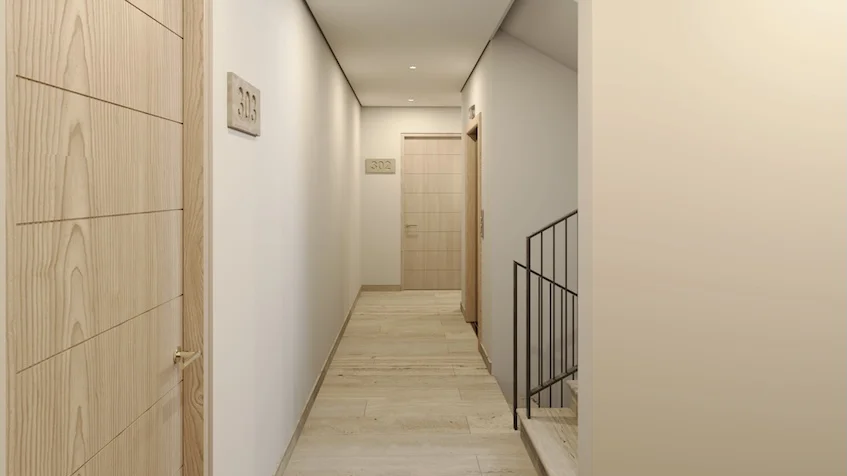 Pasillo interior iluminado con piso de duela clara puertas de madera señalizadas con números de departamento en las paredes y una barandilla metálica de escaleras en el costado derecho de Village Blu Puerto Morelos
