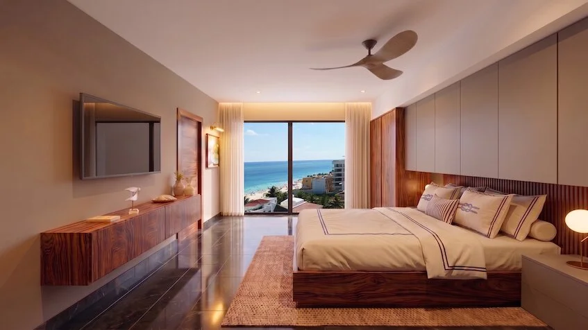 Recámara principal que incluye una cama con ropa blanca, una mesa de televisión de madera, un ventilador de techo, grandes ventanales y una vista panorámica al mar de Sensum Puerto Morelos