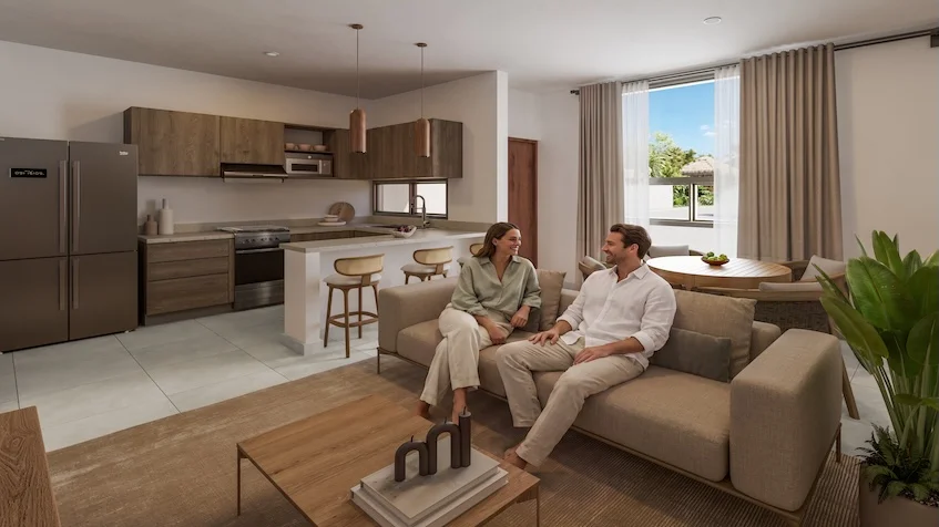 Vista interior que incluye una sala de estar con un sofá beige, una mesa de centro de madera, un área de comedor con mesa y sillas, y una cocina abierta con gabinetes de madera de The Origin by Gran Selva Puerto Morelos.