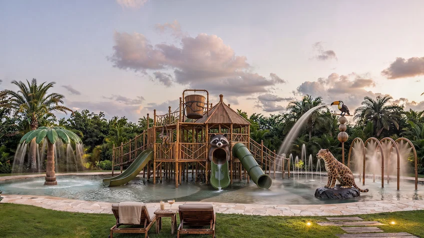 Área de juegos acuáticos infantiles con temática de selva, chorros de agua, estructuras de madera y zona de camastros, parte de las amenidades familiares del desarrollo residencial Entre Bosques Mayakobá en Playa del Carmen.