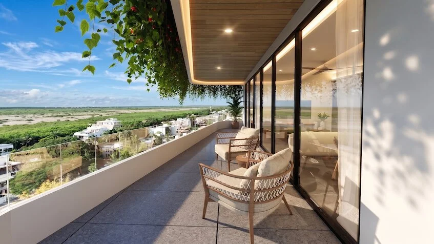 Vista de terraza lateral que incluye un área de descanso con sillones exteriores, barandanal de cristal y una vista panorámica hacia la zona urbana y vegetación de Sensum Puerto Morelos