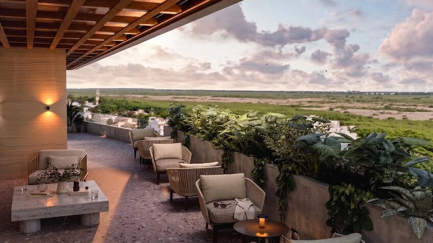 Vista de terraza que incluye un área de descanso con mesas y sillones exteriores, macetas con plantas tropicales y una vista panorámica hacia la selva y el horizonte de Sensum Puerto Morelos