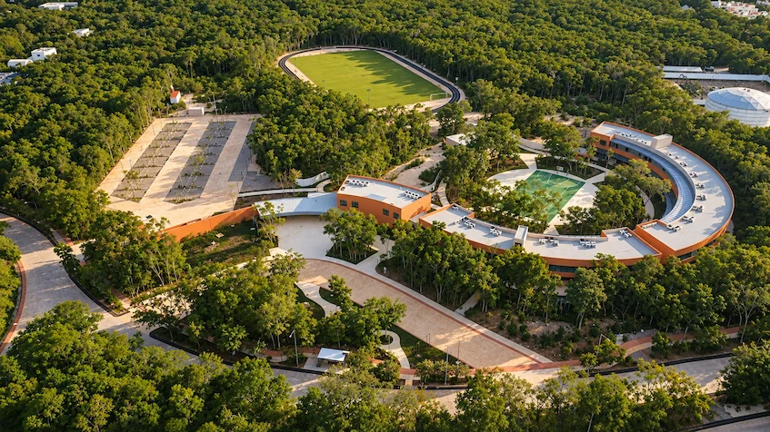 Vista aérea de las amenidades del desarrollo residencial destacando un diseño arquitectónico curvo con alberca central, áreas recreativas, canchas deportivas y amplios senderos rodeados de selva de 