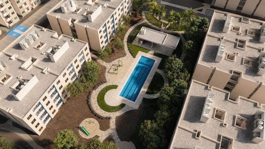 Vista aérea que incluye edificios residenciales, una alberca central, áreas verdes, una casa club y andadores peatonales de Vía Verde Playa del Carmen.